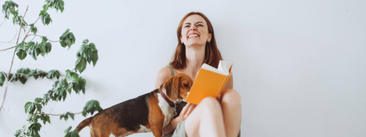 une femme lit un livre orange un chien lit avec elle . cela la fait rire !