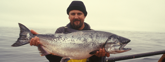 un pécheur sur un bateau, il a un énorme saumon dans les bras