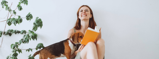 une femme lit un livre orange un chien lit avec elle . cela la fait rire ! 